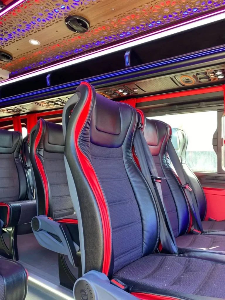 Rows of black and red leather seats inside a luxury minivan with a decorative patterned ceiling and ambient lighting