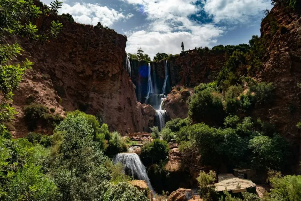 Multi-tiered Ouzoud waterfalls cascading down a red rock gorge, surrounded by green trees and cliffside terraces