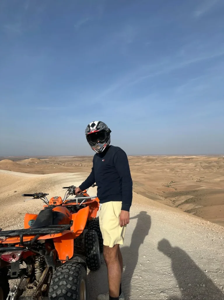 Man wearing a helmet standing next to an orange quad bike overlooking the rocky desert hills near Marrakech